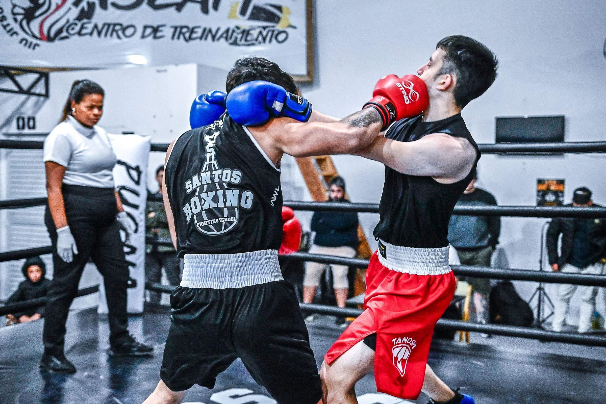 Combate de boxe no ringue da Santos Boxing, colete Santos Boxing e shorts vermelhos