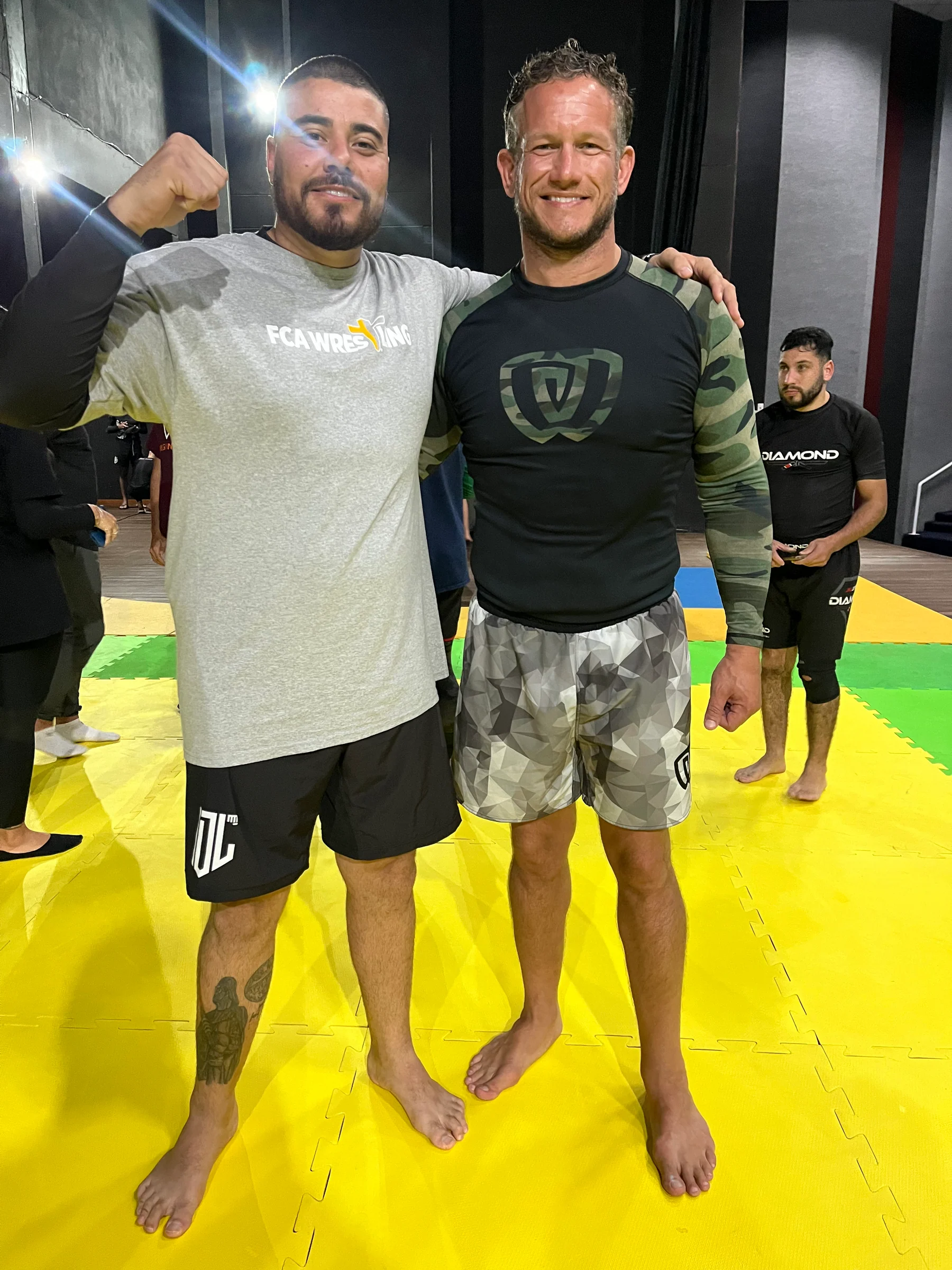 Duas pessoas no tatame amarelo da Team Santos, fora da sala de kimono